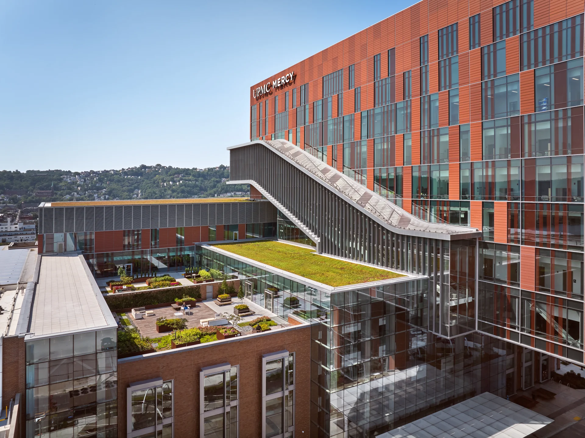 Rooftop terrace at the UPMC Vision and Rehabilitation Hospital at UPMC Mercy featuring landscaped seating areas, a green roof, and an elevated connector structure adjacent to the patient tower.